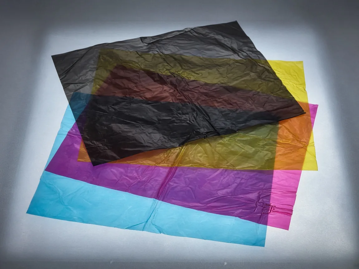 Four translucent sheets, cyan, magenta, yellow, and black, stacked so the overlaps look darker.