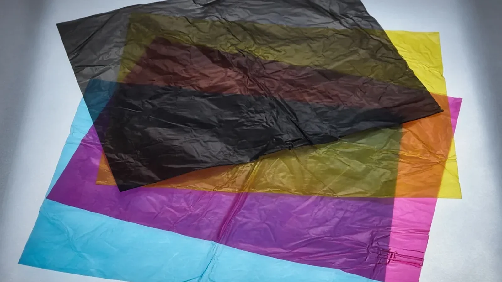 Four translucent cyan, magenta, yellow, and black separation sheets stacked on an illuminated surface showing darker overlapping areas